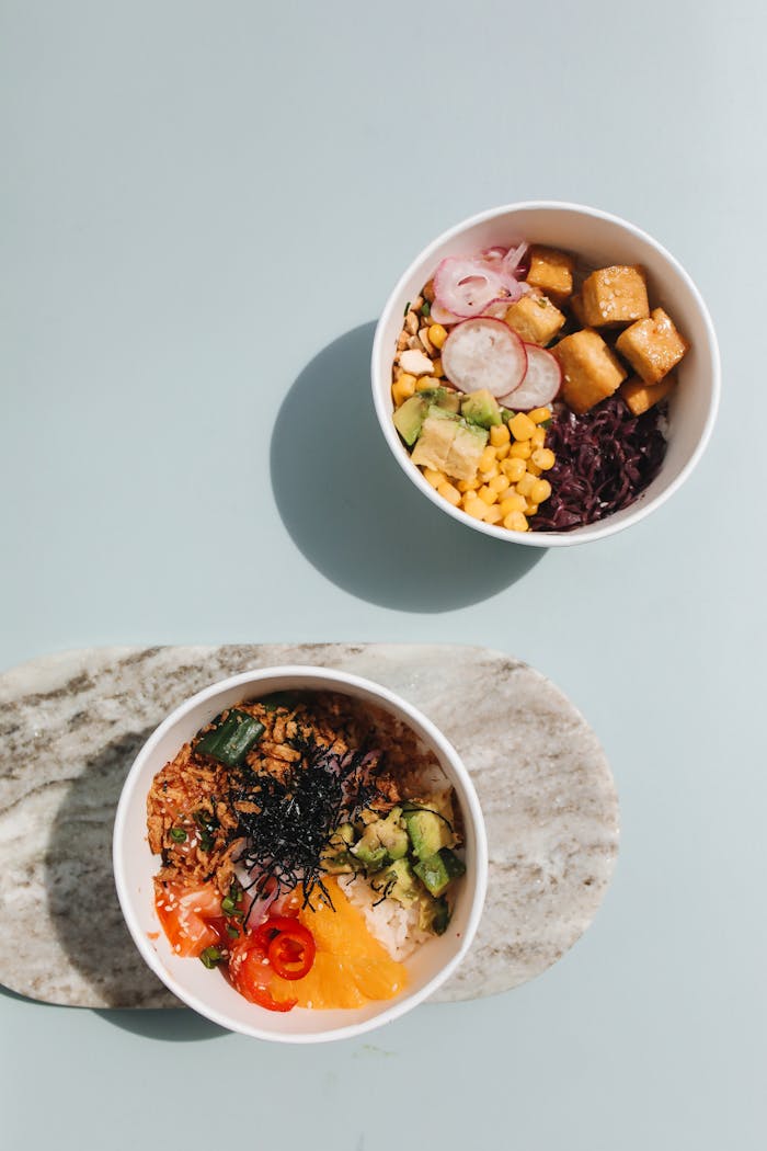 Overhead view of delicious poke bowls featuring fresh tofu, seaweed, and vegetables on a light background.